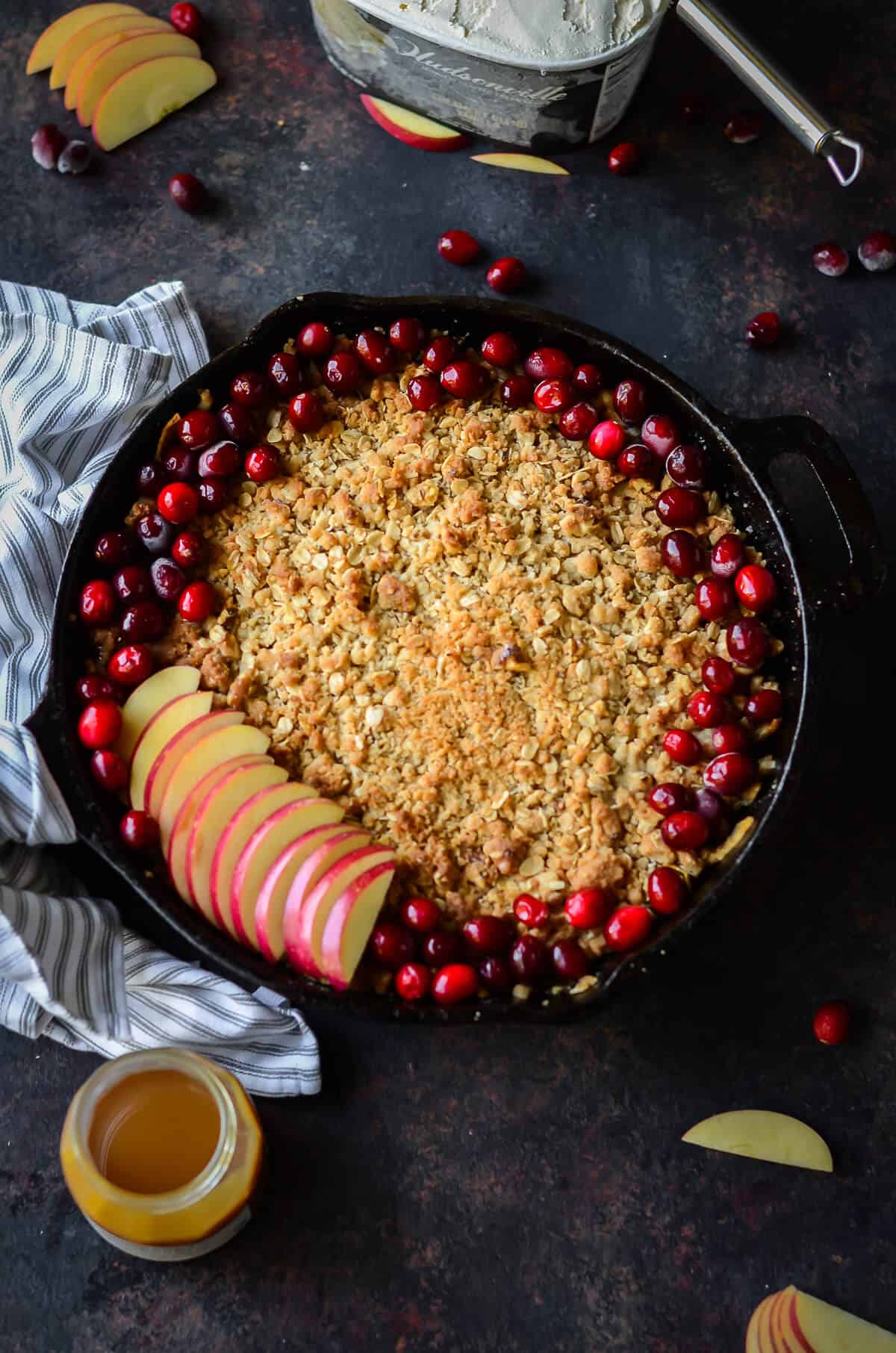 healthy apple crisp baked in a cast iron skillet topped with fresh cranberries and fresh apples