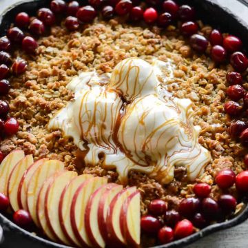 Maple apple crisp baked in a cast iron skillet topped with 3 scoops of vanilla ice cream, fresh cranberries, fresh apples and salted caramel drizzle