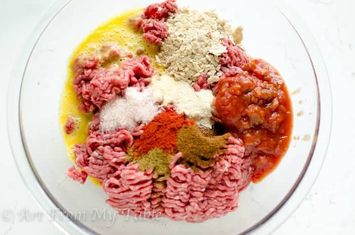 Ingredients for meatloaf partially mixed in a bowl: ground beef, spices, salsa and egg.