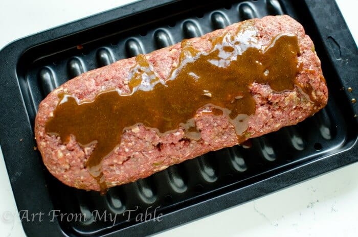 Low-carb Mexican meatloaf on a broiler pan, prior to cooking, topped with enchilada sauce.