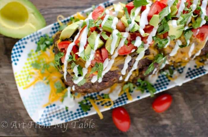 Top view of Low-carb Mexican meatloaf on a platter topped with cheese, cilantro, tomato and avocado.