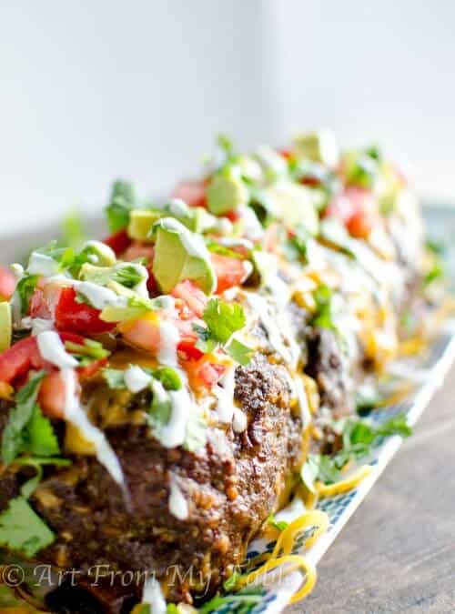 Low carb Mexican meatloaf on a platter, topped with tomatoes, avocados, cilantro and sour cream.