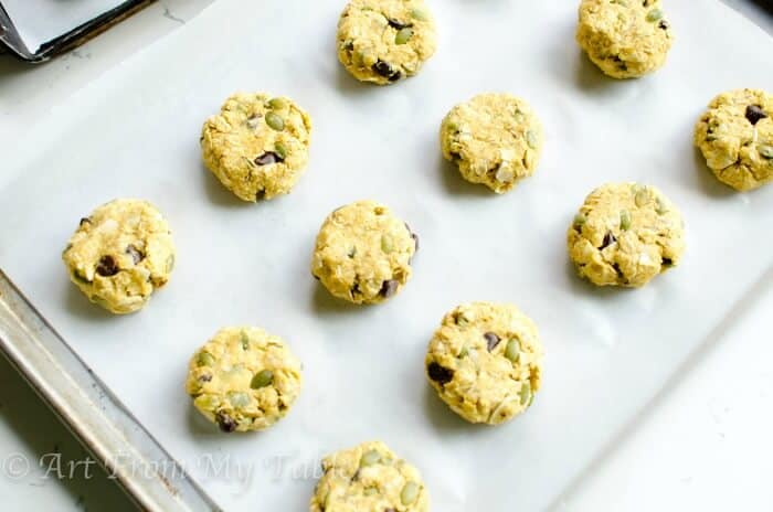 Pre-cooked Pumpkin breakfast cookies, slightly flattened, on a baking sheet lined with parchment paper.