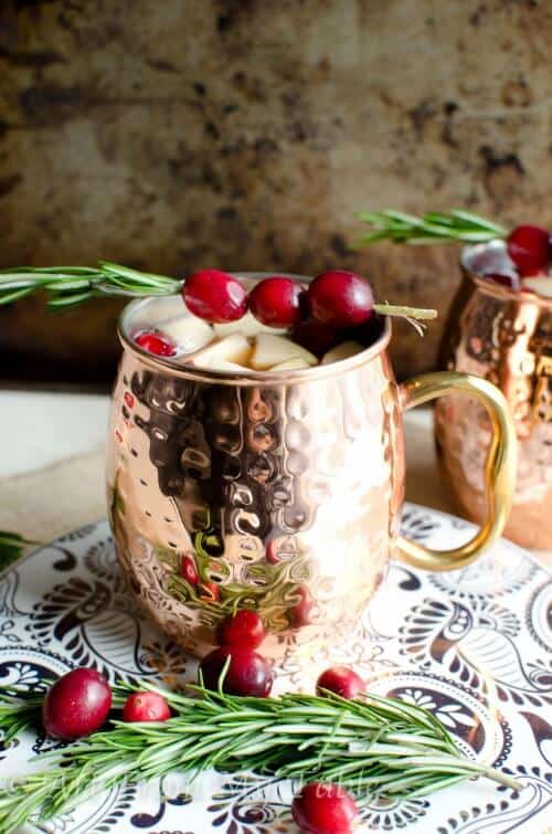 Sparkling cider sangria (nonalcoholic) in a copper mug garnished with rosemary and fresh cranberries.