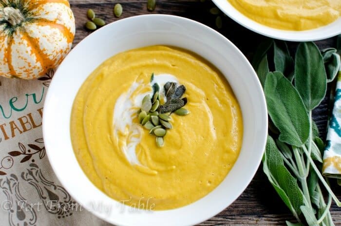 Bowl of smoky pumpkin soup garnished with sour cream, pepitos and crispy fried sage.
