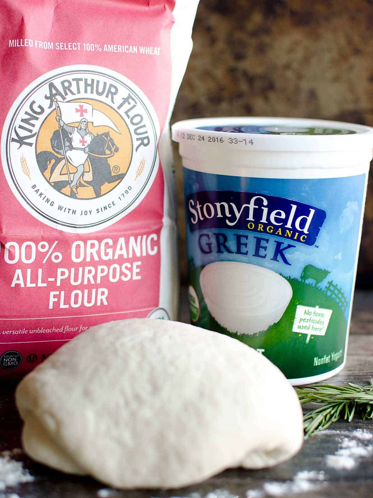 Bag of King Arthur Flour and a quart of Stonyfield Greek yogurt, with a ball of pizza dough.