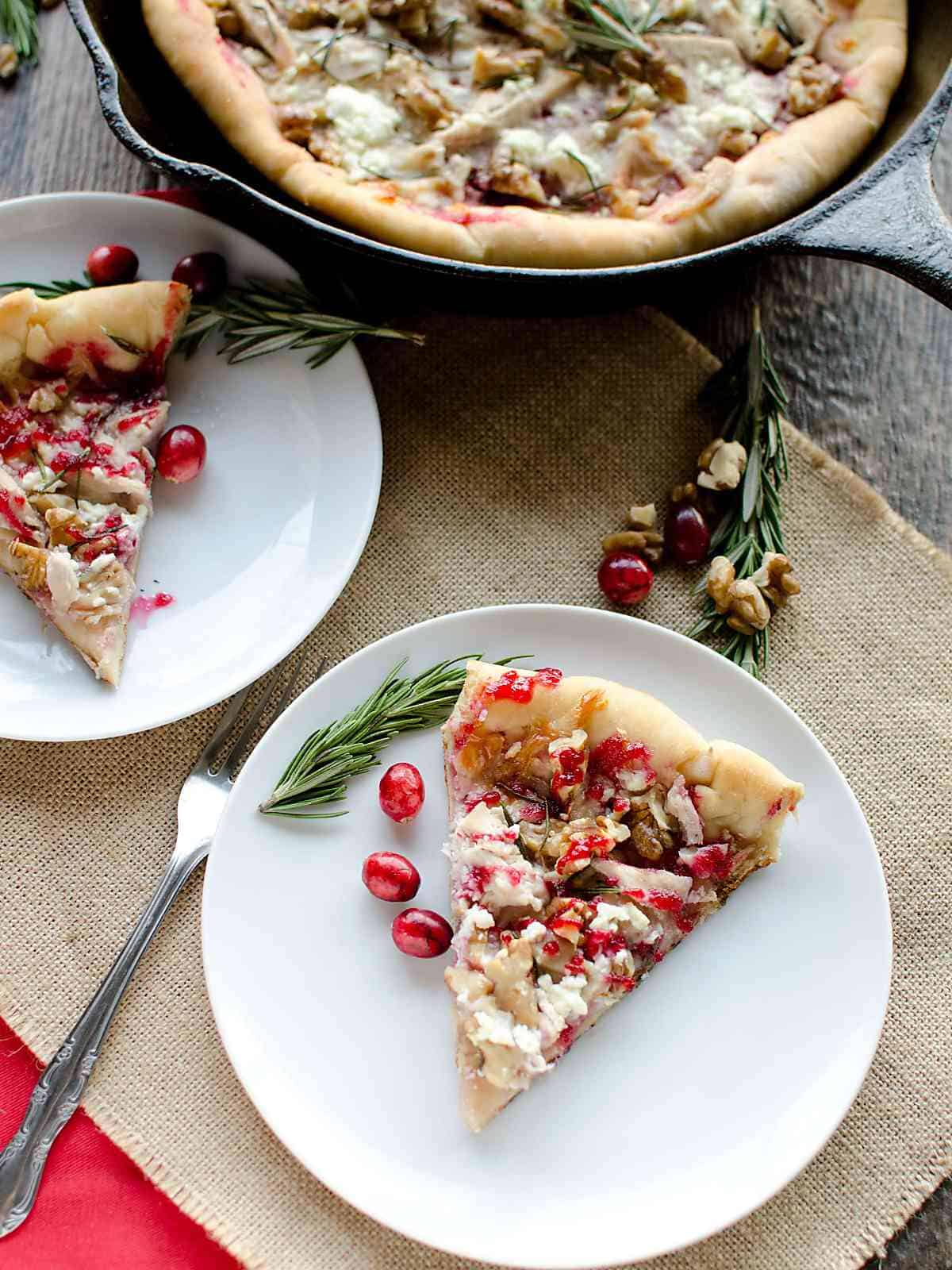 2 plates with slices of Turkey cranberry pizza and fresh rosemary, remainder of the pizza in the background.
