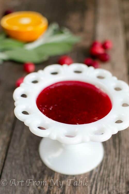 Homemade cranberry sauce in a serving dish, fresh orange half and cranberries in the background.