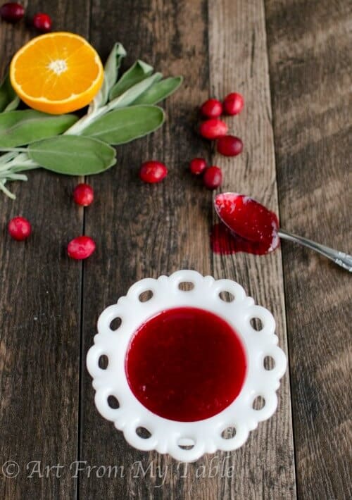 Homemade cranberry sauce in a white bowl, spoon on the side.