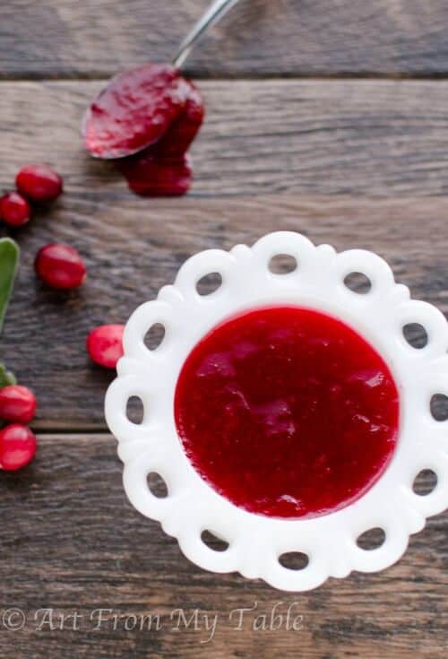 Homemade cranberry sauce in a serving dish, fresh cranberries scattered around the dish.