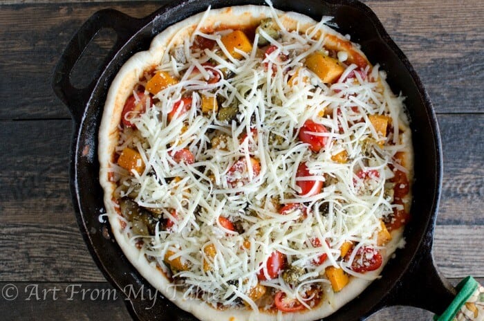 Pizza with sausage and roasted vegetables and cheese, just before baking in a cast iron pan.