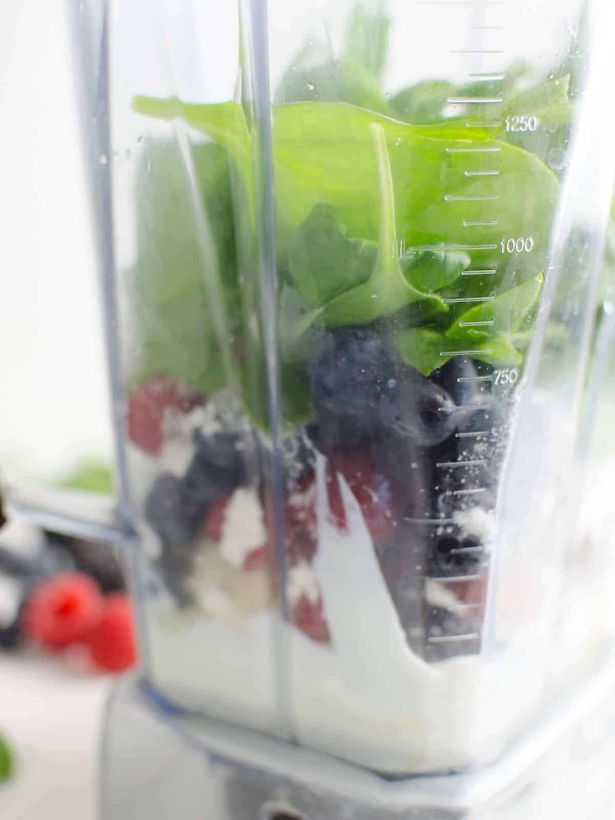 Spinach, berries, yogurt, and other smoothie ingredients in a blender prior to blending.