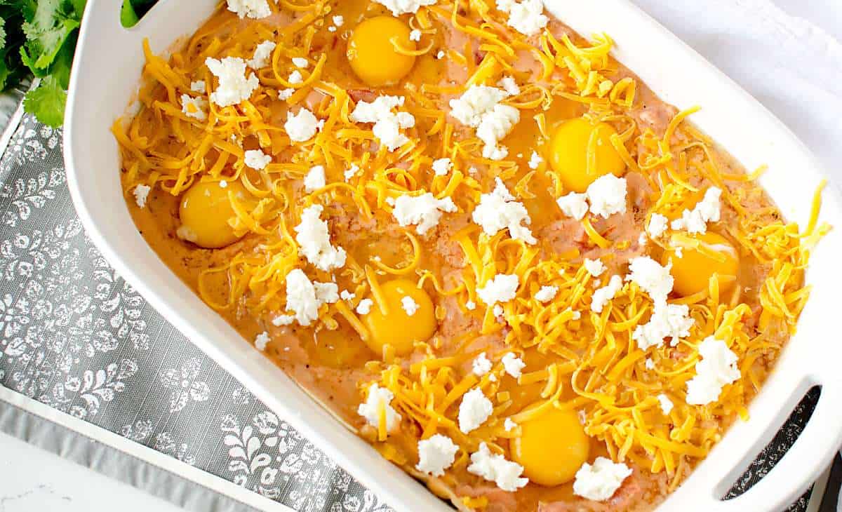uncooked eggs on top of tomato cream sauce topped with cheddar and goat cheese, before baking. 
