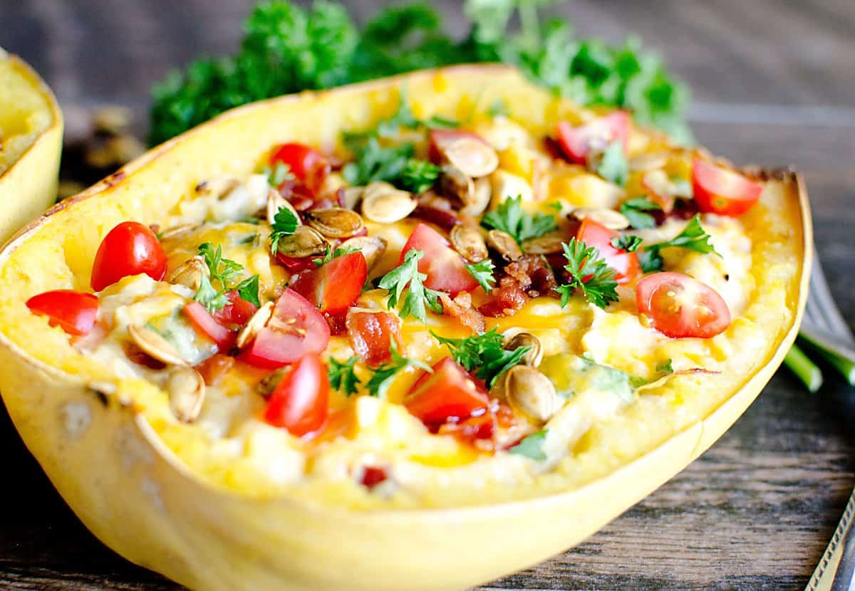 loaded spaghetti squash casserole boat topped with tomatoes, parsley, and toasted squash seeds.