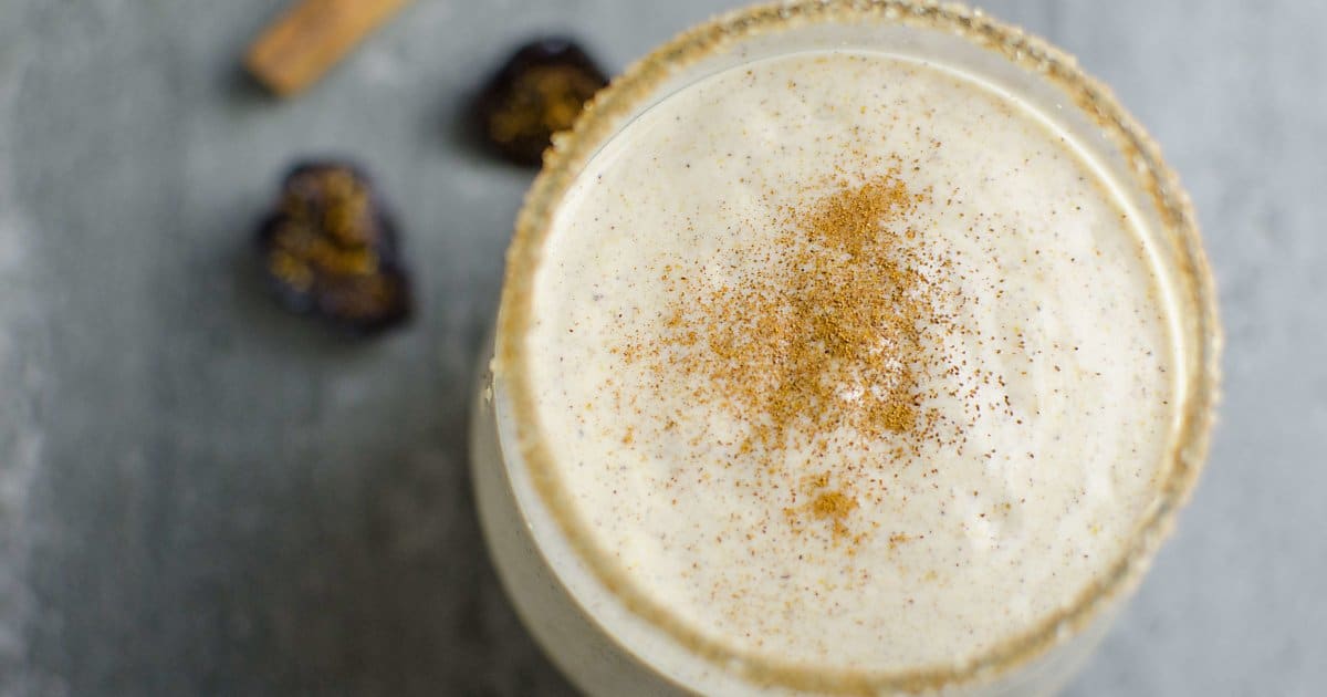 looking down into a glass full of fig newton smoothie sprinkled with cinnamon. The rim of the glass is covered in sugar, a few figs and cinnamon stick next to the glass.