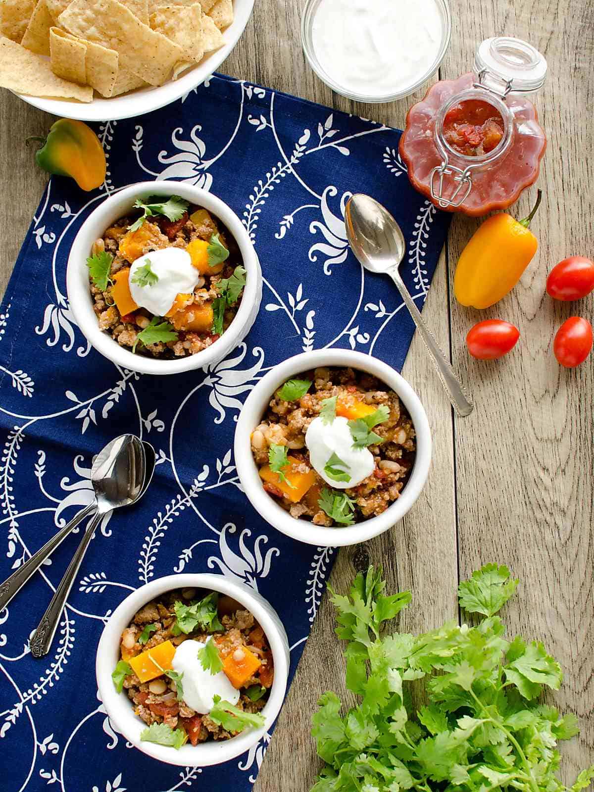 3 bowls of turkey chili with butternut squash garnished with sour cream and cilantro.