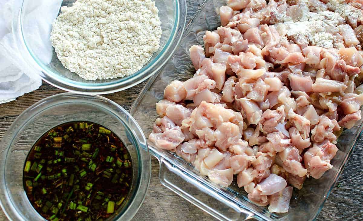 dish of diced raw chicken, bowl gluten free flour (baking mix) and bowl of orange chicken sauce.