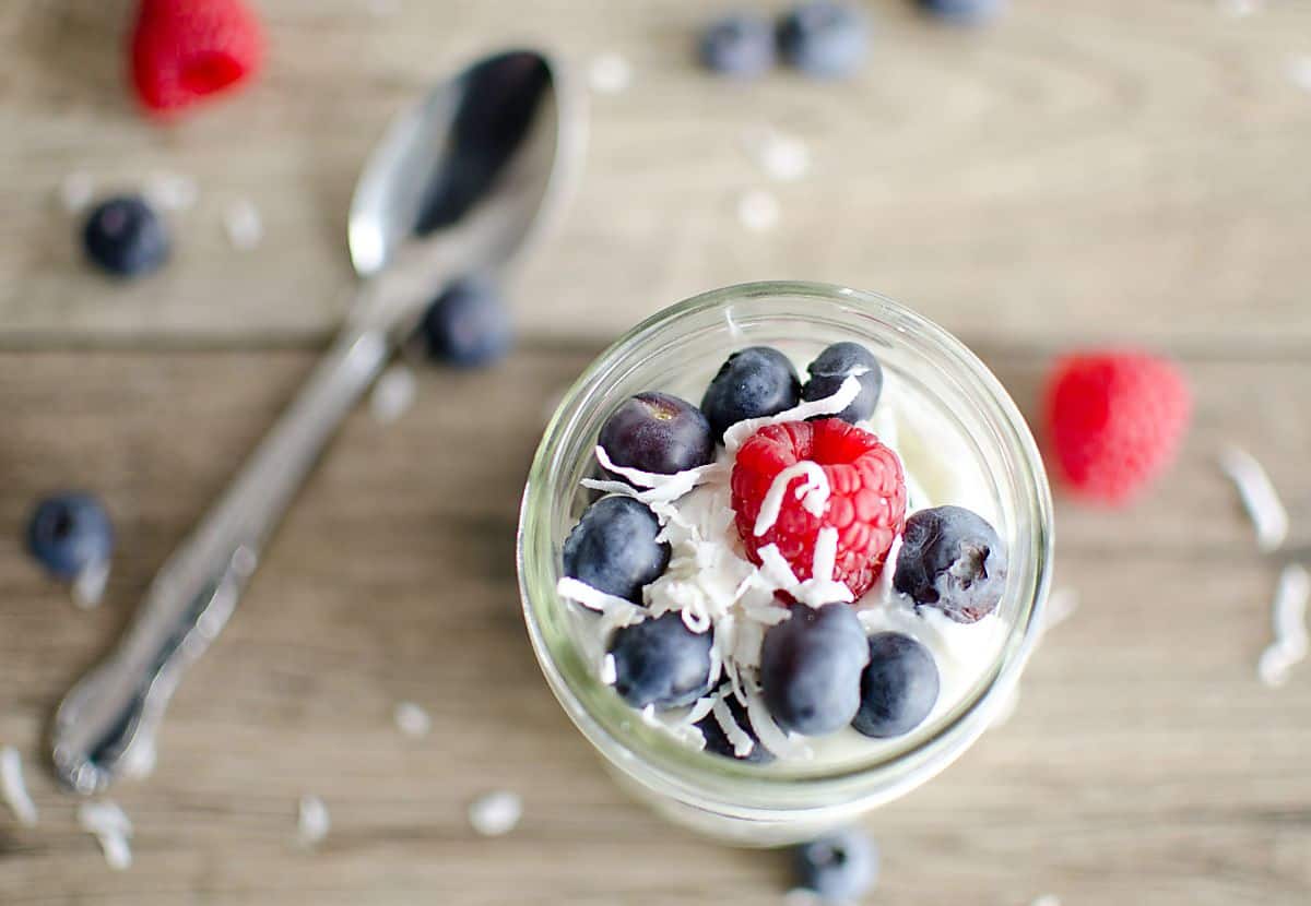 yogurt parfait with coconut yogurt, blueberries and raspberries garnished with shredded coconut.