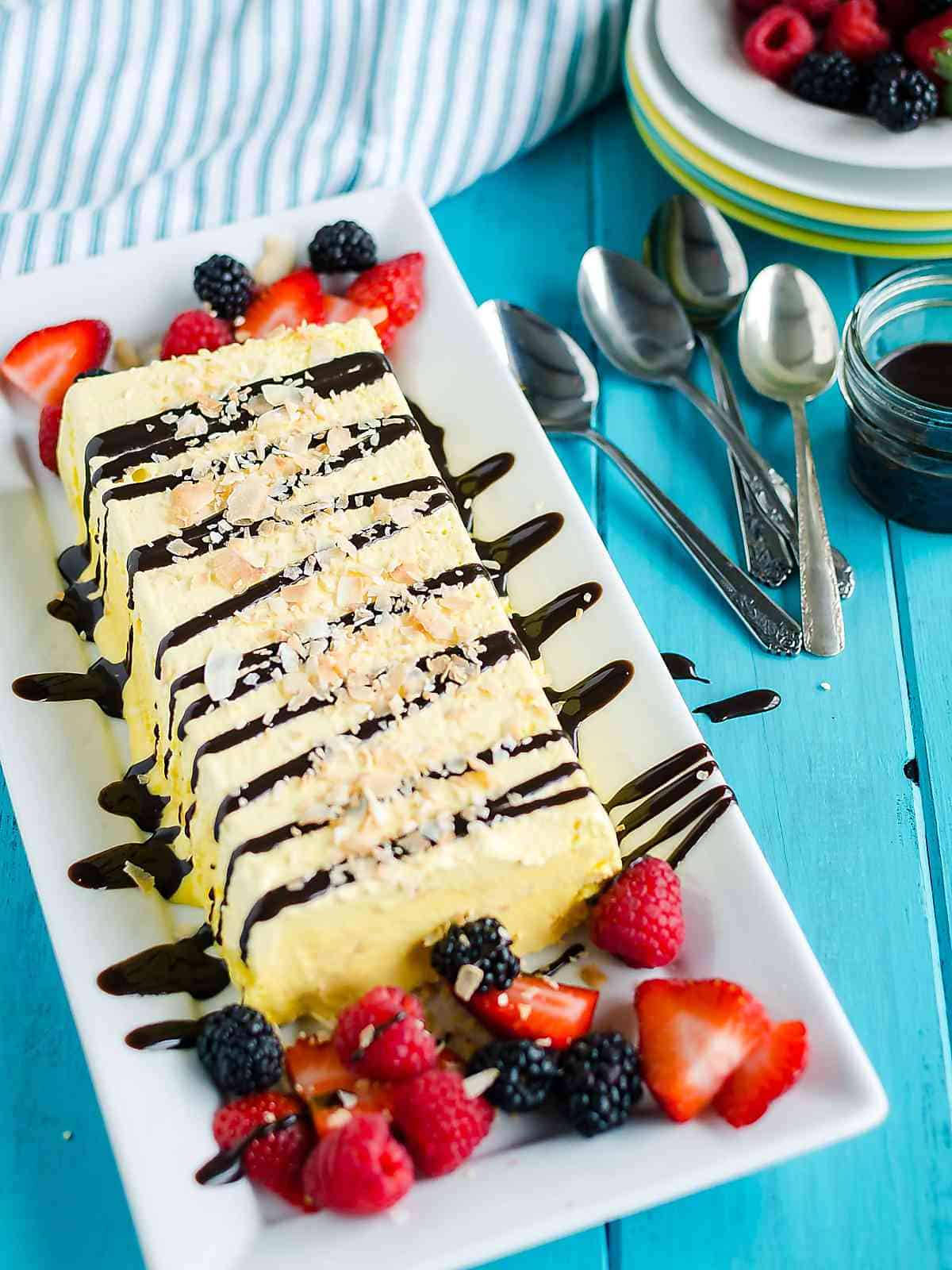 traditional French parfait frozen dessert on a rectangular white platter, drizzled with chocolate syrup, garnished with toasted coconut chips.
