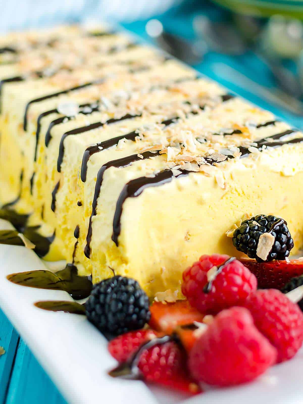 traditional French parfait frozen dessert. Displayed on a platter in the shape of a rectangle/loaf. This one is flavored with coconut, drizzled with chocolate and garnished with fresh berries.
