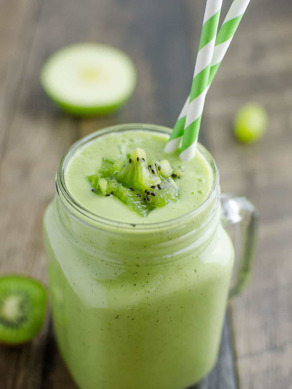 healthy green smoothie garnished with bits of kiwi in a glass jar mug.
