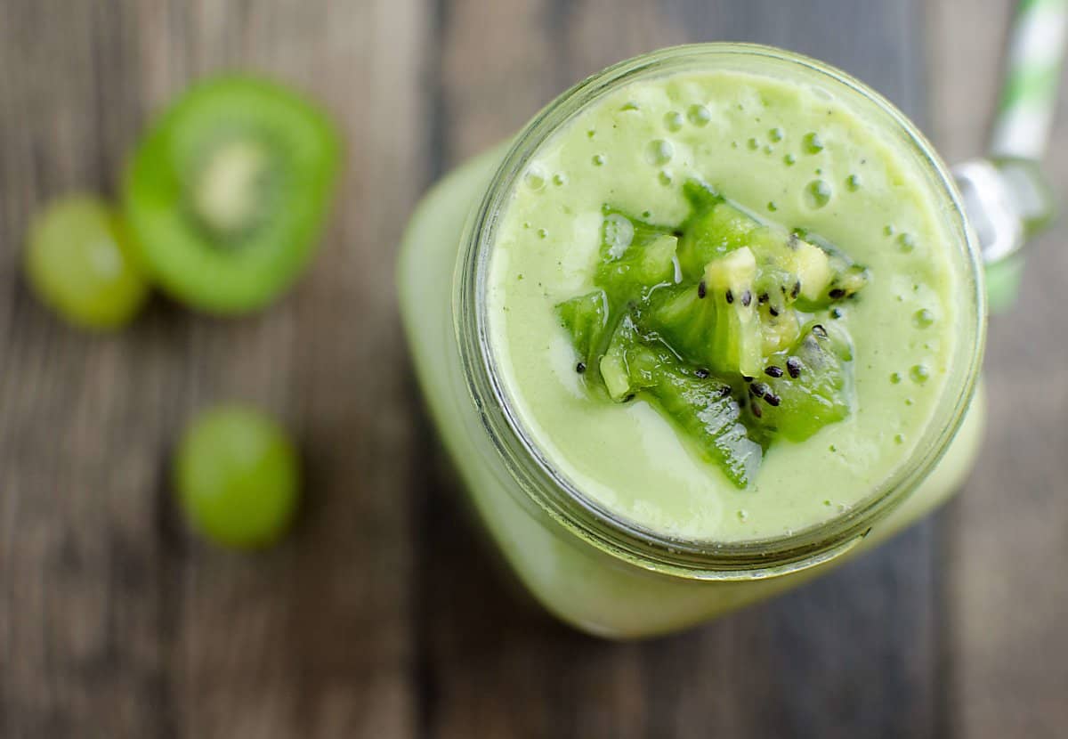 Top view of a frothy green smoothie garnished with chunks of kiwi.