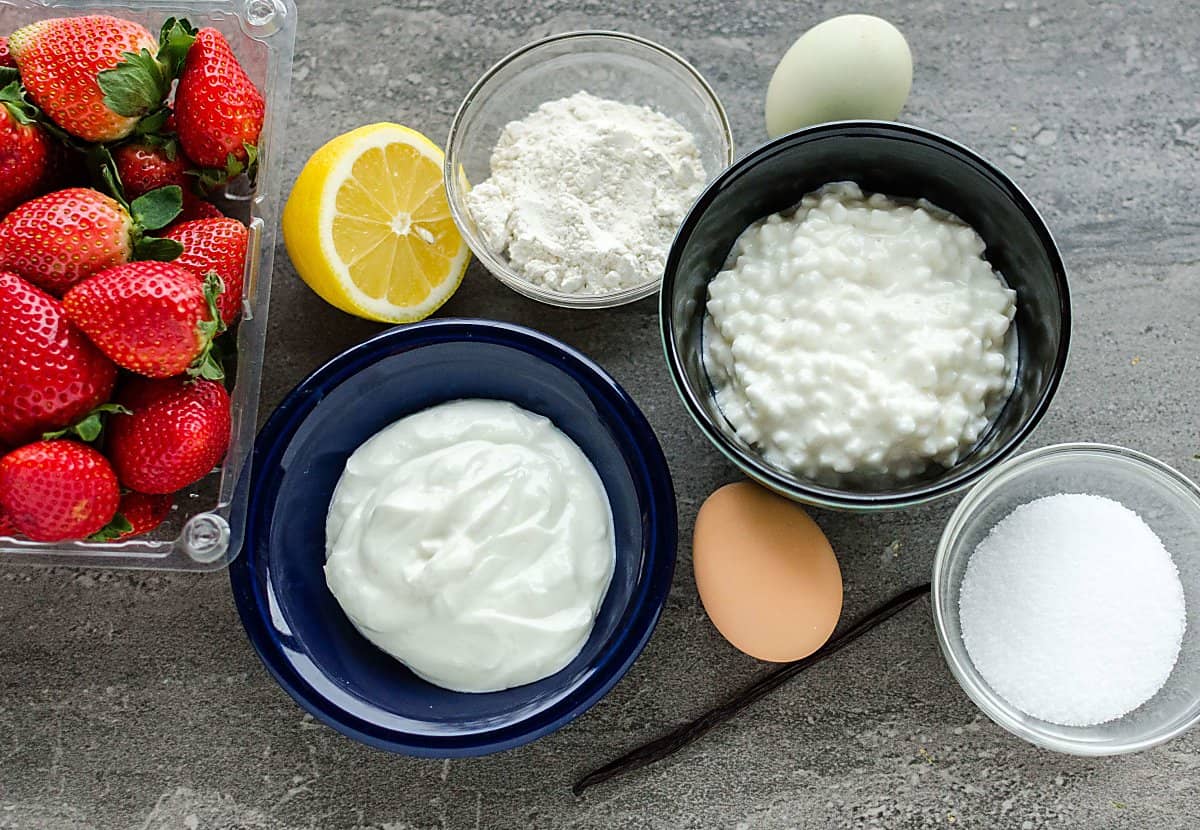ingredients for a lightened up version of cheesecake: Yogurt, cottage cheese, flour, sugar, lemon, eggs, strawberries, vanilla bean.