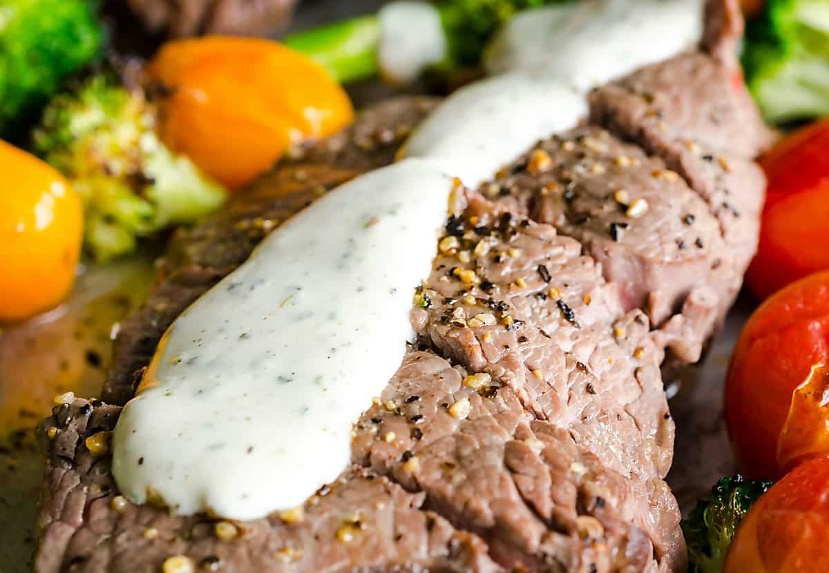 close up image of homemade Boursin cheese sauce on top of a seasoned sliced cooked steak.