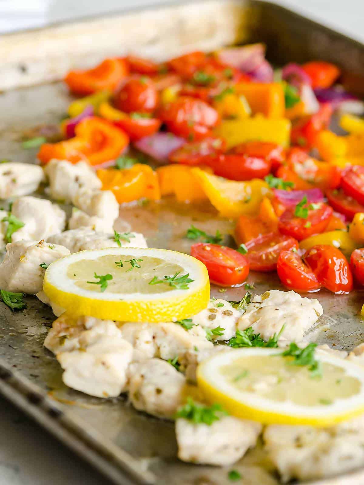 Greek chicken sheet pan dinner- diced chicken, peppers, onions, tomatoes, lemon slices cooked on a sheet pan, garnished with fresh parsley.