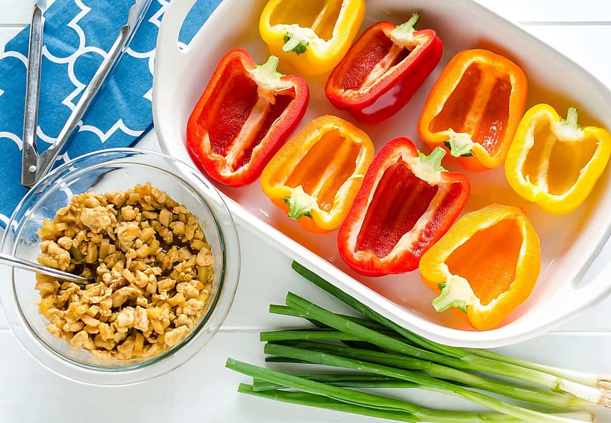 9x13 dish filled with colored bell peppers sliced in half. Bowl of Asian chicken diced for filling the pepprs with. Scallions on the side.