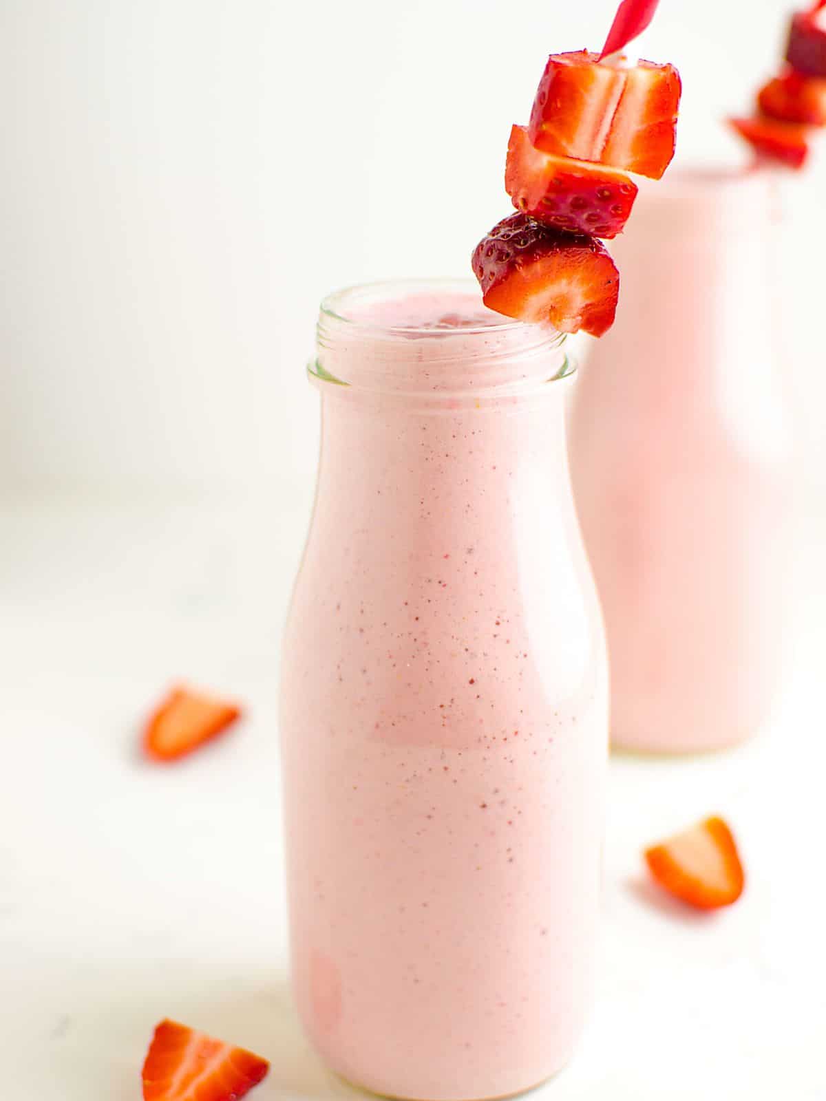 2 milk bottle glasses filled with a strawberry smoothie, garnished with fresh strawberries on the straw. 