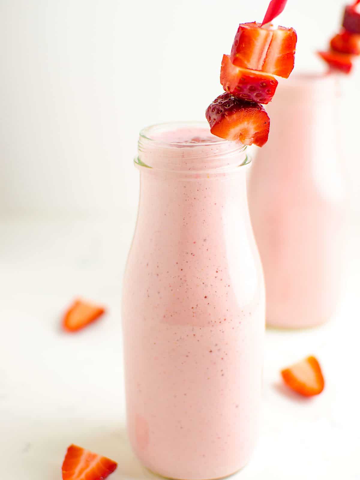 2 milk bottle glasses filled with a strawberry smoothie, garnished with fresh strawberries on the straw.