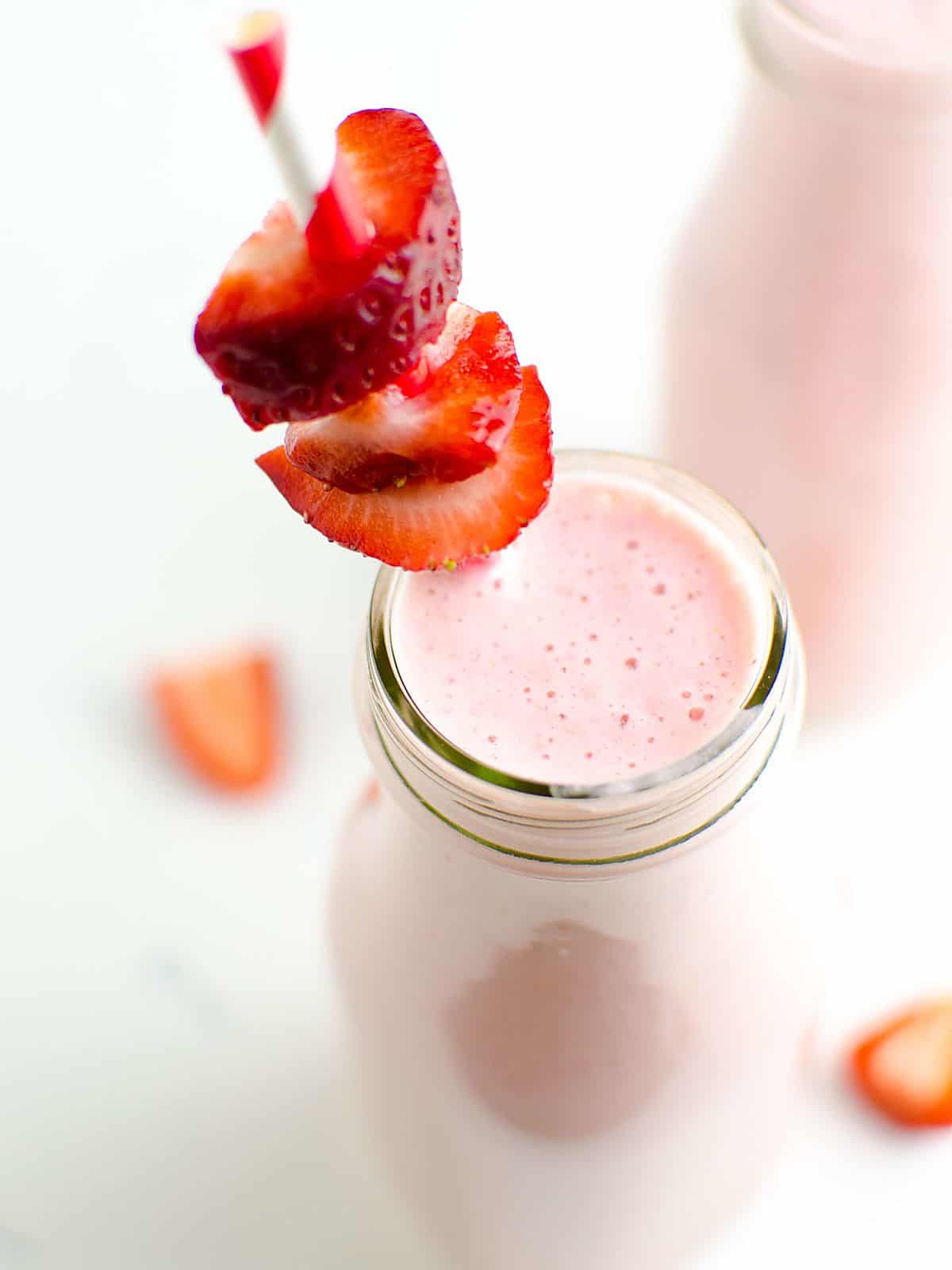 strawberry protein shake in a  glass garnished with fresh strawberries.