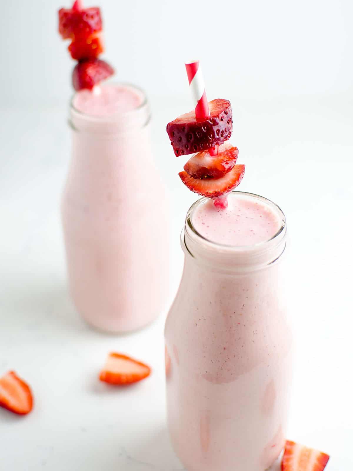 Strawberry cheesecake protein smoothie in a milk bottle glass garnished with sliced strawberries on a straw.