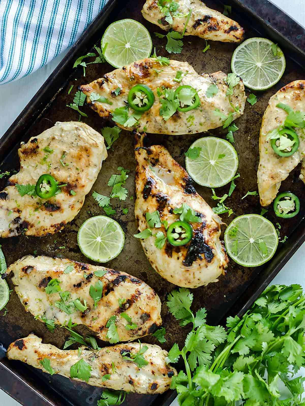 marinated grilled chicken breasts on a sheet pan with lime slices, cilantro and jalapeno.