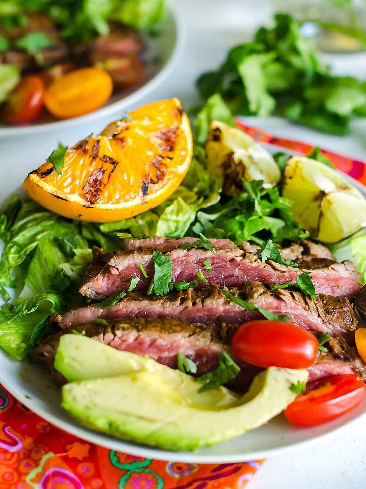grilled carne asada on a plate garnished with orange and lime wedges