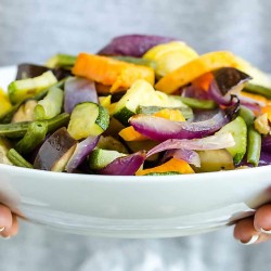 hands holding a white bowl full of colorful roasted vegetables