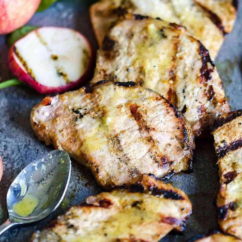 group of grilled boneless pork chops with grilled apples and mustard sauce drizzled over top