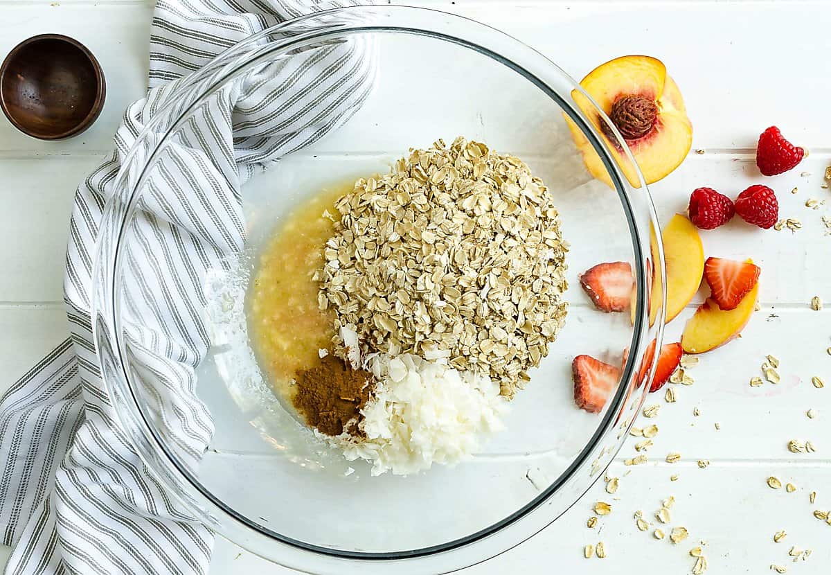 clear mixing bowl with rolled oats, mashed banana, cinnamon, and coconut flakes