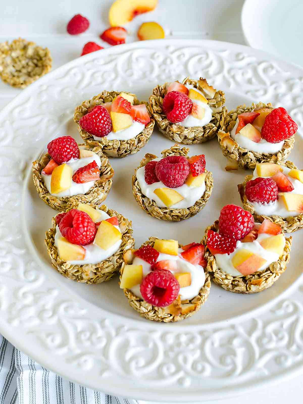 white platter of coconut granola cups filled with yogurt, peaches and raspberries