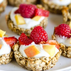 granola cup filled with yogurt, peaches, strawberries and rasbperries