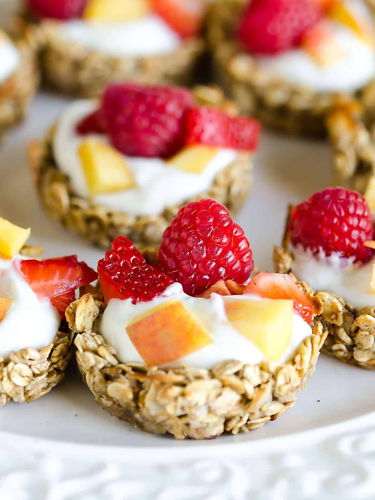 granola cup filled with yogurt, peaches, strawberries and rasbperries