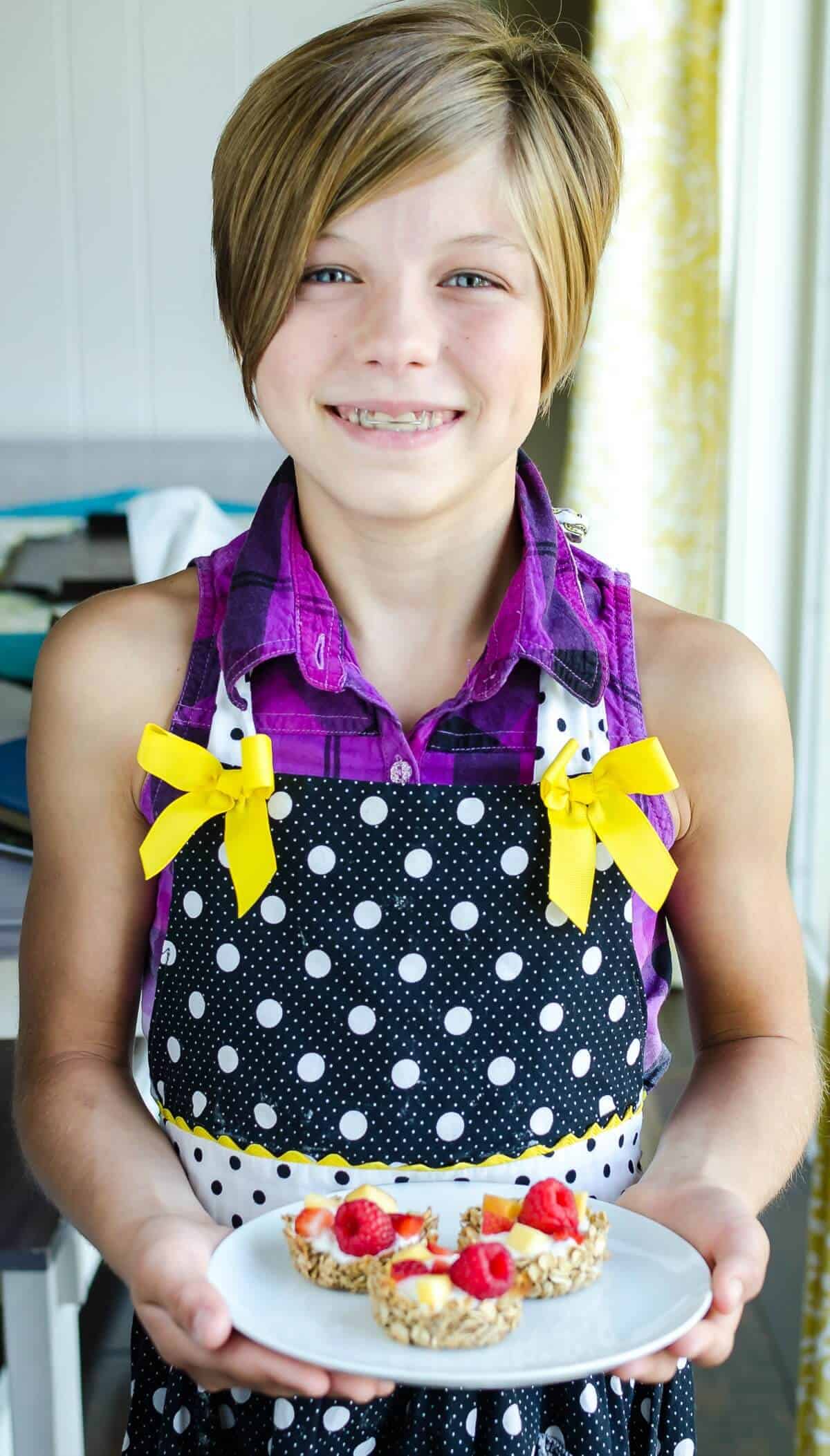 young girl holding plate of breakfast granola cups filled with yogurt and fruit