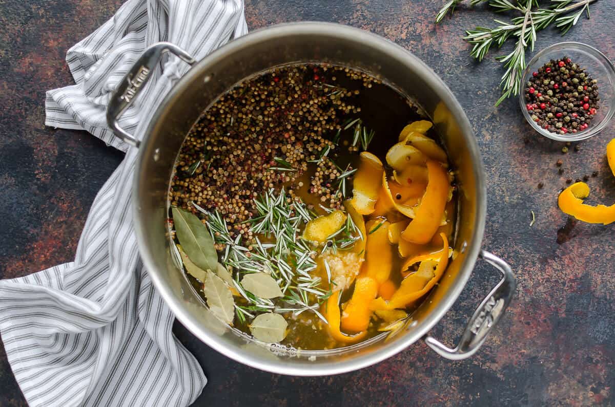 overhead view of turkey brine containing water, salt, apple cider orange peels, fresh herbs and whole tri-color peppercorns