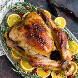 overhead view of the best roast turkey recipe on a platter surrounded with orange slices, rosemary, and fresh cranberries