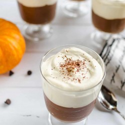 chocolate mousse with pumpkin whipped cream in a clear glass stemmed serving glass with several others in the background