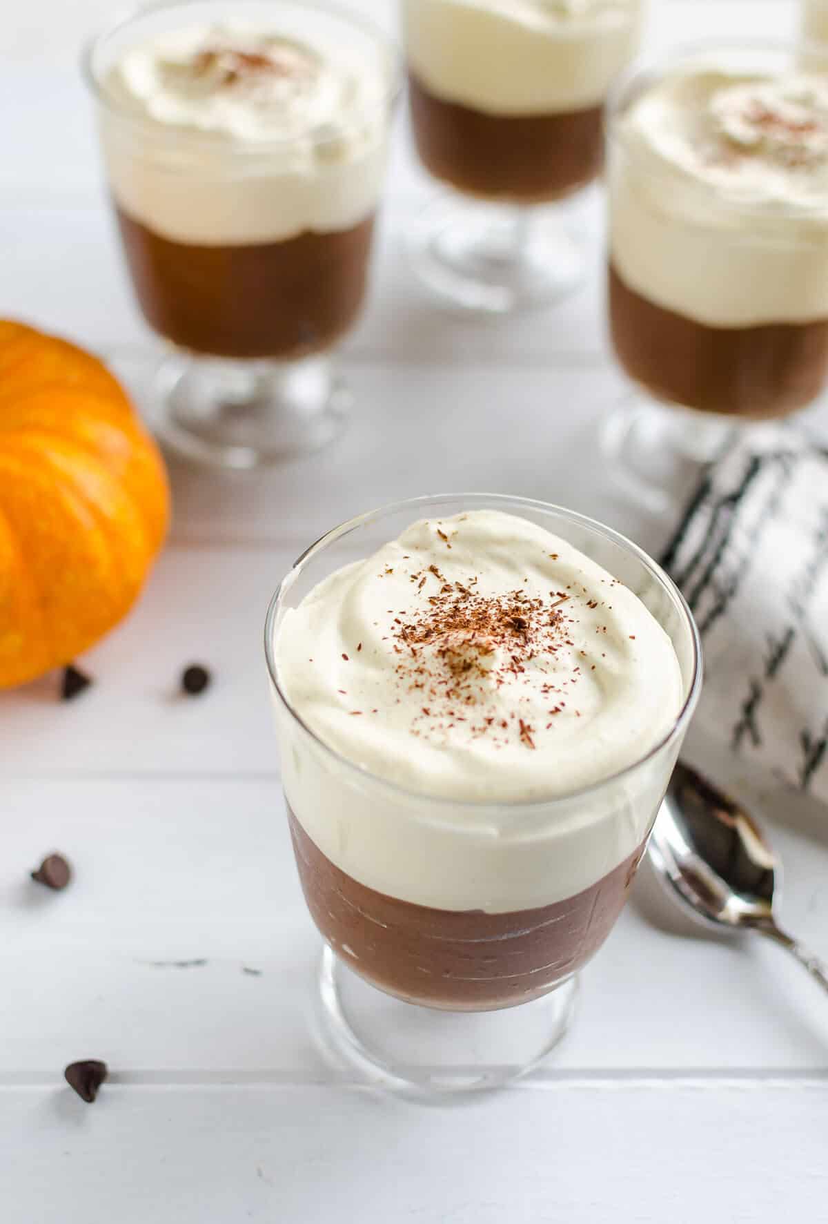chocolate mousse with pumpkin whipped cream in a clear glass stemmed serving glass with several others in the background