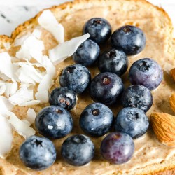 whole grain toast topped with almond butter, section of coconut flakes, section of fresh blueberries, section of almonds