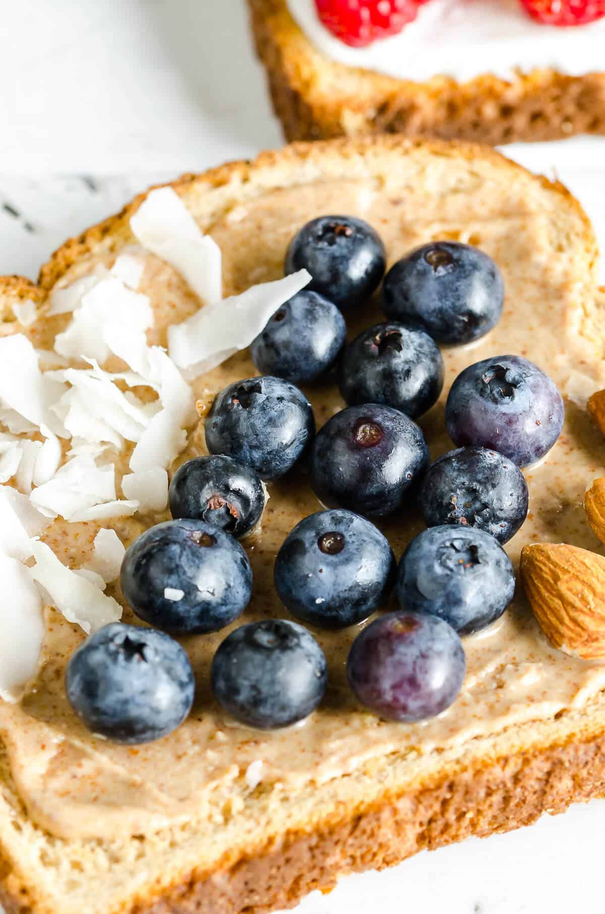 whole grain toast topped with almond butter, section of coconut flakes, section of fresh blueberries, section of almonds