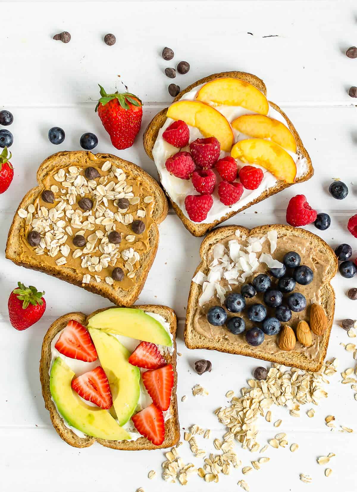 4 breakfast toast ideas, 1 slice with peanut butter, rolled oats and chocolate chips, 1 with yogurt, honey, fresh raspberries and fresh peaches, 1 with almond butter, coconut and fresh blueberries, 1 with cream cheese, avocado slices, and sliced strawberries